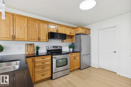 Kitchen featuring wood-finish cabinetry, dark countertops, and stainless steel appliances - 64 Foxboro Link, Sherwood Park, AB - Indoor Photo Showing Kitchen With Double Sink