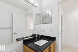 Bathroom vanity featuring a light wood-finish cabinet with black hardware, black countertop, and an integrated white sink with chrome faucet - 