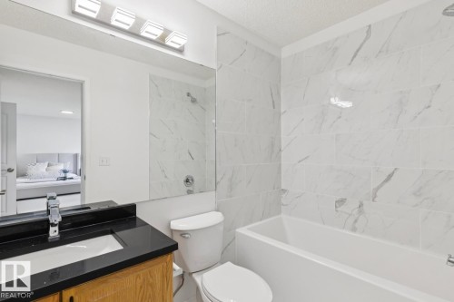 Contemporary bathroom featuring a white tile shower surround with gray veining, a white built-in bathtub, and a wood-finish vanity with a black countertop and integrated sink - 64 Foxboro Link, Sherwood Park, AB - Indoor Photo Showing Bathroom