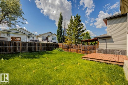 Expansive backyard featuring a large green lawn, a wooden fence, mature trees, and a ground-level deck - 64 Foxboro Link, Sherwood Park, AB - Outdoor