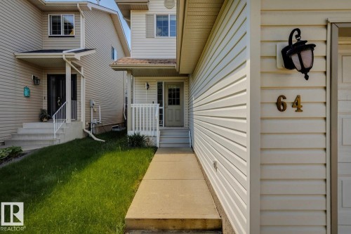 Cream-colored vinyl siding exterior featuring a covered front entry, concrete walkway, and an attached outdoor wall lantern - 64 Foxboro Link, Sherwood Park, AB - Outdoor With Exterior