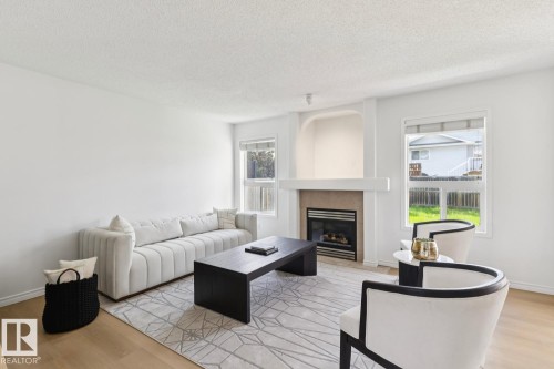 Living area featuring light wood-finish flooring, white walls, and a fireplace with a light-colored mantel and hearth - 64 Foxboro Link, Sherwood Park, AB - Indoor Photo Showing Living Room With Fireplace