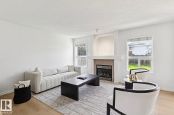 Living area featuring light wood-finish flooring, white walls, and a fireplace with a light-colored mantel and hearth - 