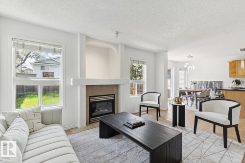 Living area featuring a gas fireplace with tile surround, adjacent windows, and wood-finish flooring - 64 Foxboro Link, Sherwood Park, AB - Indoor Photo Showing Living Room With Fireplace