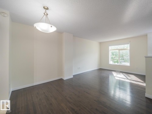 Spacious room featuring dark wood-finish flooring, light-toned walls, white baseboards, a large window, and a contemporary ceiling light fixture - #66 465 Hemingway Rd Nw, Edmonton, AB - Indoor Photo Showing Other Room