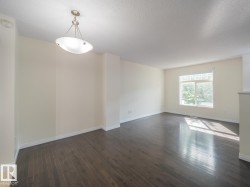 Spacious room featuring dark wood-finish flooring, light-toned walls, white baseboards, a large window, and a contemporary ceiling light fixture - 