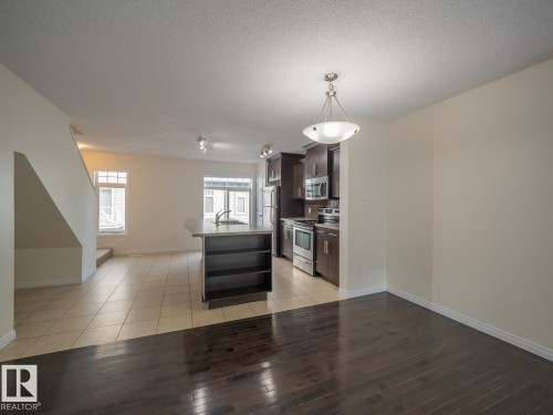 Open-concept living area featuring a kitchen island with built-in shelving, stainless steel appliances, dark wood-finish cabinetry, and a combination of tile and dark wood-finish flooring - #66 465 Hemingway Rd Nw, Edmonton, AB - Indoor