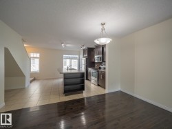 Open-concept living area featuring a kitchen island with built-in shelving, stainless steel appliances, dark wood-finish cabinetry, and a combination of tile and dark wood-finish flooring - 