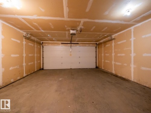 Attached single-bay garage featuring an automatic overhead door, concrete flooring, and unfinished drywall walls and ceiling - #66 465 Hemingway Rd Nw, Edmonton, AB - Indoor Photo Showing Garage
