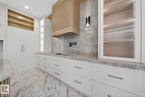 Kitchen featuring light wood-finish range hood, white cabinetry with contemporary hardware, and fluted glass upper cabinets - 11 Harley Way, Spruce Grove, AB - Indoor