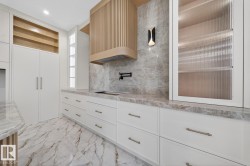 Kitchen featuring light wood-finish range hood, white cabinetry with contemporary hardware, and fluted glass upper cabinets - 