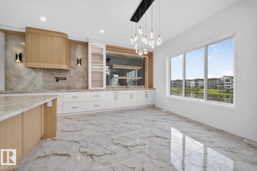 Spacious kitchen area featuring large format marble-look floor tiles, white cabinetry with contemporary hardware, and a wood-finish island with a stone countertop - 11 Harley Way, Spruce Grove, AB - Indoor Photo Showing Kitchen