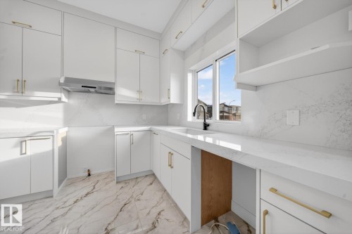 Modern kitchen featuring white cabinetry with gold-tone hardware, white countertops, a deep undermount sink with a black faucet, and a coordinating white tile backsplash - 11 Harley Way, Spruce Grove, AB - Indoor Photo Showing Kitchen