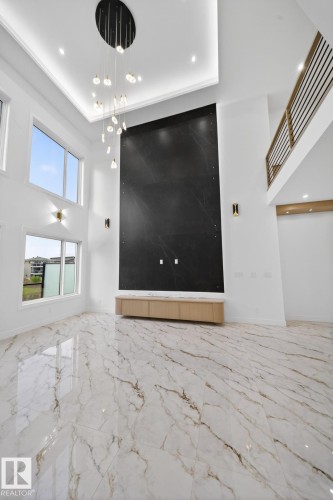 High-ceiling living area featuring large format marble-look floor tiling, a dramatic dark accent wall, and a contemporary multi-pendant chandelier - 11 Harley Way, Spruce Grove, AB - Indoor Photo Showing Other Room