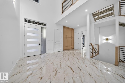 Two-story foyer featuring large format marble-look tile flooring, a modern entry door with frosted glass panels and transom window, and a wood-finish staircase with contemporary black metal railings - 11 Harley Way, Spruce Grove, AB - Indoor Photo Showing Other Room