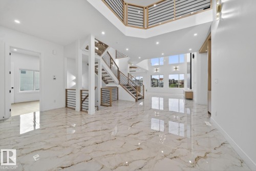 Spacious open-concept interior featuring high ceilings, large format marble-look tile flooring, and a multi-level staircase with wood-tone treads and horizontal metal railings - 11 Harley Way, Spruce Grove, AB - Indoor Photo Showing Other Room