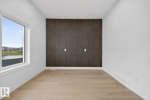 Accent wall with geometric paneling, light wood-finish flooring, white baseboards, and a large window - 11 Harley Way, Spruce Grove, AB - Indoor Photo Showing Other Room