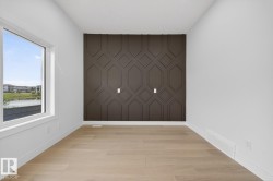 Accent wall with geometric paneling, light wood-finish flooring, white baseboards, and a large window - 
