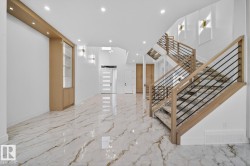Grand entrance featuring polished floor tile with marble-effect veining, a built-in display cabinet with interior lighting, and a modern staircase with wood handrails and black metal balusters - 