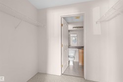Carpeted room with wire shelving, offering direct access to a bathroom featuring a toilet, vanity with a light wood-finish cabinet, and a wall-mounted light fixture - 