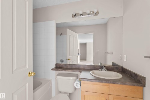 Bathroom featuring a wood-finish vanity with a built-in sink, a large wall-mounted mirror, and a white tiled shower/tub combination - #224 16303 95 St Nw, Edmonton, AB - Indoor Photo Showing Bathroom