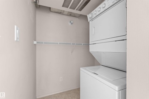 Dedicated laundry space featuring a white stacked washer and dryer unit, wire shelving, and neutral wall tones - #224 16303 95 St Nw, Edmonton, AB - Indoor Photo Showing Laundry Room