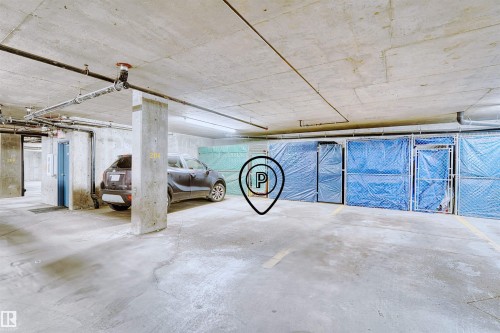 Concrete underground parking garage featuring exposed ceilings, overhead lighting, and dedicated storage units - #224 16303 95 St Nw, Edmonton, AB - Indoor Photo Showing Garage
