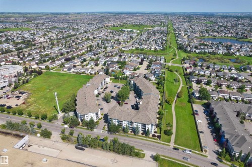 Expansive residential area featuring a large undeveloped green space, a multi-building apartment complex with parking, and a paved roadway - #224 16303 95 St Nw, Edmonton, AB - Outdoor With View