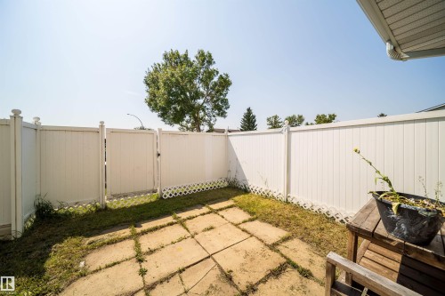 Fully fenced backyard featuring a patio area with square pavers, a white vinyl fence, and a gate - 11432 139 Avenue Nw, Edmonton, AB - Outdoor