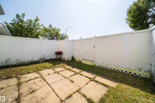 Enclosed outdoor space featuring a white privacy fence, concrete patio pavers, and a grass area - 11432 139 Avenue Nw, Edmonton, AB - Outdoor