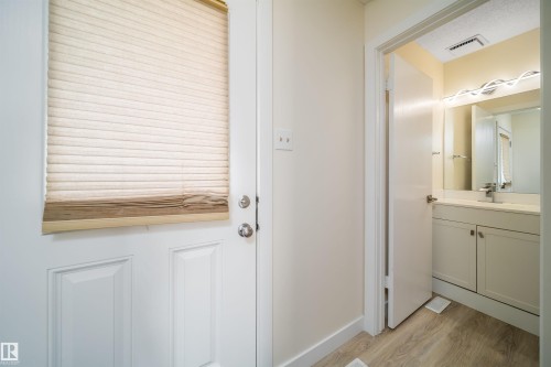 Panel door with privacy blind and an adjacent bathroom featuring a vanity with white cabinetry, light-toned countertop, and a contemporary light fixture - 11432 139 Avenue Nw, Edmonton, AB - Indoor