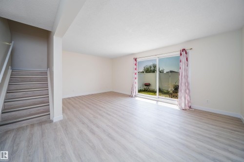 Open-concept living space featuring light wood-finish flooring, white walls, and a staircase with a light wood-finish handrail - 11432 139 Avenue Nw, Edmonton, AB - Indoor Photo Showing Other Room