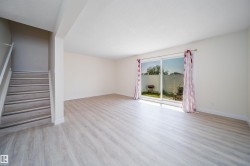 Open-concept living space featuring light wood-finish flooring, white walls, and a staircase with a light wood-finish handrail - 