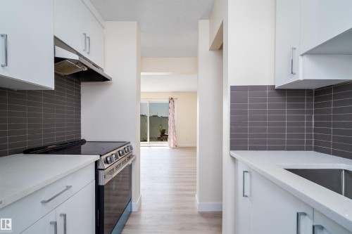 Modern kitchen featuring white cabinetry, stainless steel range with overhead hood, light-toned countertops, and a subway tile backsplash - 11432 139 Avenue Nw, Edmonton, AB - Indoor Photo Showing Kitchen