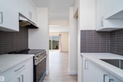 Modern kitchen featuring white cabinetry, stainless steel range with overhead hood, light-toned countertops, and a subway tile backsplash - 