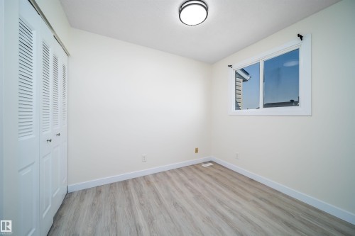 Neutral-toned interior featuring wood-finish flooring, white baseboards, and a white window frame - 11432 139 Avenue Nw, Edmonton, AB - Indoor Photo Showing Other Room