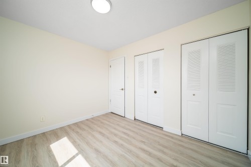 Neutral wall paint, wood-finish flooring, two sets of bi-fold louvered closet doors, and a flush-mount ceiling light - 11432 139 Avenue Nw, Edmonton, AB - Indoor Photo Showing Other Room