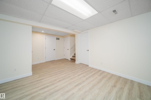 Spacious room featuring light wood-finish flooring, white walls, and a drop ceiling with integrated lighting - 11432 139 Avenue Nw, Edmonton, AB - Indoor Photo Showing Other Room