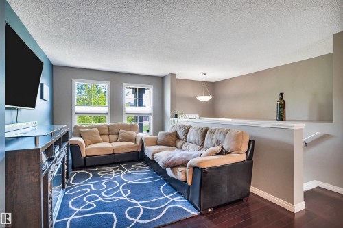 Spacious living area featuring dark wood-finish flooring, ample natural light from multiple windows, a contemporary light fixture, and a partial wall with a cap - 571 Orchards Boulevard Sw, Edmonton, AB - Indoor Photo Showing Living Room