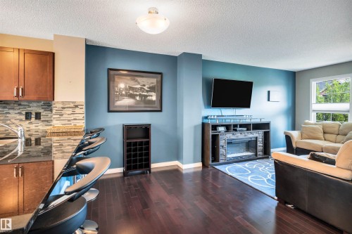 Open-concept living space with dark wood-finish flooring, and a window with exterior greenery visible - 571 Orchards Boulevard Sw, Edmonton, AB - Indoor Photo Showing Living Room With Fireplace
