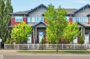 Townhome exterior featuring red and gray siding, multiple windows, and a white picket fence - 571 Orchards Boulevard Sw, Edmonton, AB  - Outdoor With Facade 