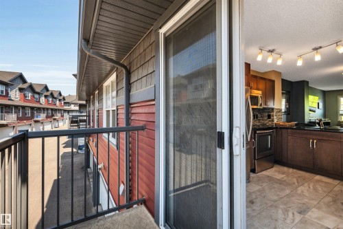 Balcony access from the kitchen, featuring sliding glass doors, a black metal railing, and a red shingle exterior - 571 Orchards Boulevard Sw, Edmonton, AB - Outdoor With Exterior