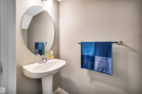 Pedestal sink with chrome faucet, complemented by an oval mirror and overhead vanity lighting - 571 Orchards Boulevard Sw, Edmonton, AB - Indoor Photo Showing Bathroom