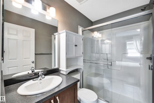 Bathroom featuring a wood-finish vanity with an oval undermount sink, dark countertop, and a chrome faucet - 571 Orchards Boulevard Sw, Edmonton, AB - Indoor Photo Showing Bathroom