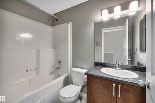 Full bathroom featuring a white tub/shower combination with chrome fixtures, a toilet, and a vanity with a dark countertop and an undermount sink - 571 Orchards Boulevard Sw, Edmonton, AB - Indoor Photo Showing Bathroom