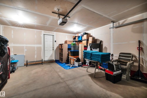Concrete floor garage with an attached garage door opener, white interior door, and exposed drywall walls - 571 Orchards Boulevard Sw, Edmonton, AB - Indoor Photo Showing Garage