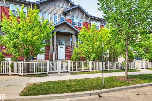 Multi-level townhome featuring a red and gray facade, a covered entry porch, and white paneled door - 571 Orchards Boulevard Sw, Edmonton, AB - Outdoor