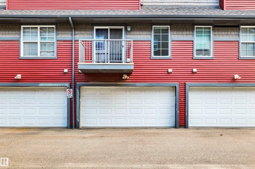 Red horizontal siding exterior with multiple white paneled garage doors - 571 Orchards Boulevard Sw, Edmonton, AB - Outdoor With Exterior