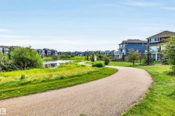 Curved gravel pathway bordering a body of water, surrounded by green grass and mature trees - 