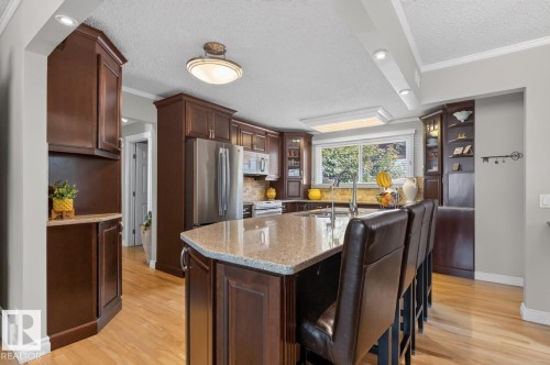 Kitchen featuring wood-finish flooring, dark wood cabinetry, stainless steel appliances, and a central island with a light-toned countertop - 27 Milford Crescent, Sherwood Park, AB - Indoor Photo Showing Kitchen